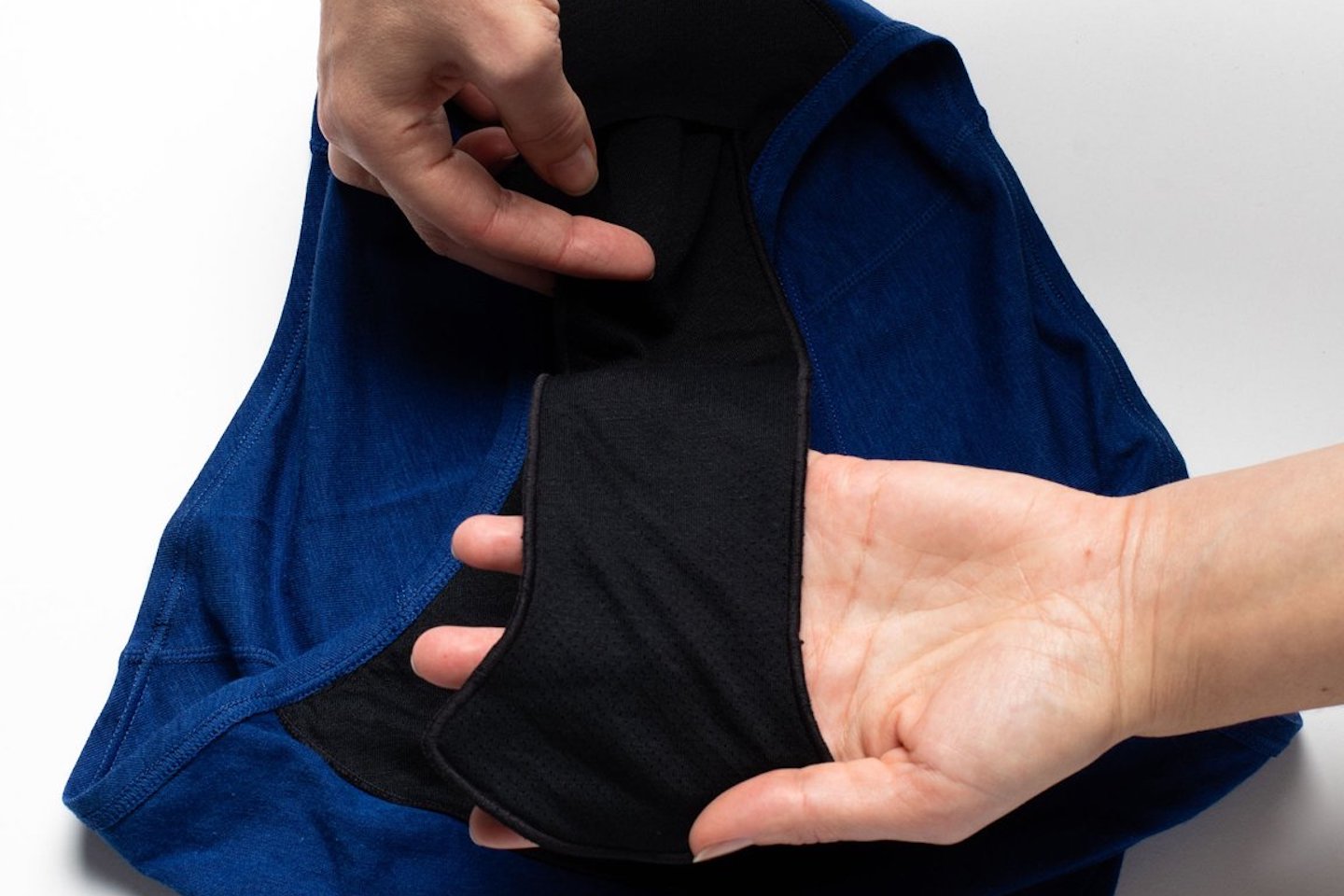 Two hands are seen inserting a black piece of fabric (named the Booster) into the gusset of a pair of period underwear. The underwear is blue.