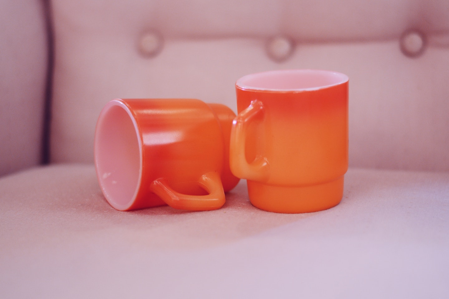 Two orange mugs are on a chair. One is laying on its side.