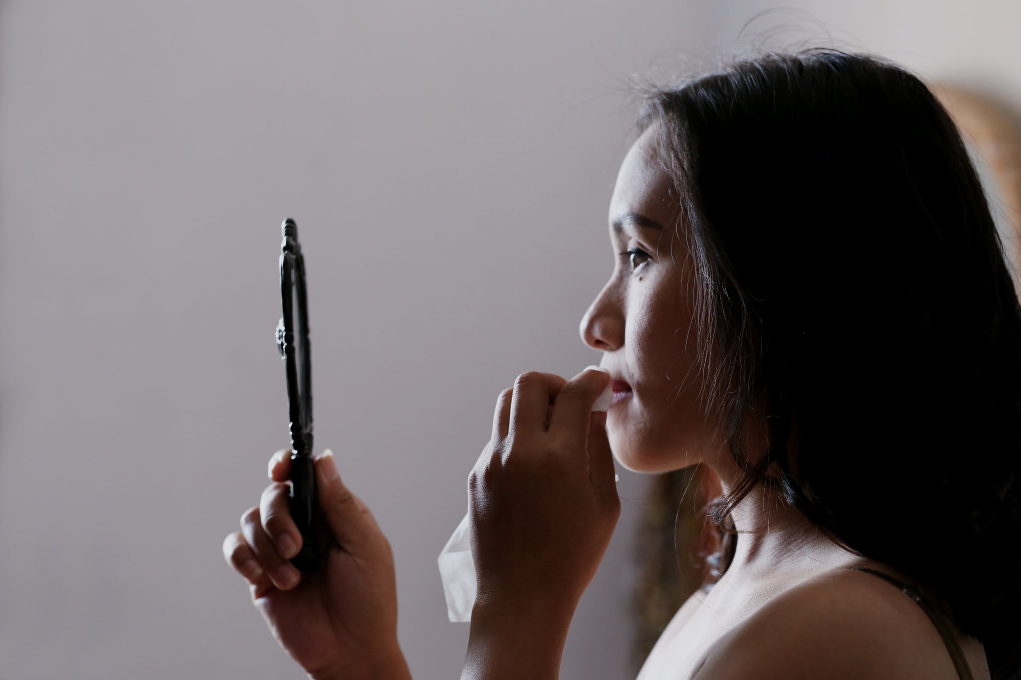 Woman removing lipstick while looking in a handheld mirror