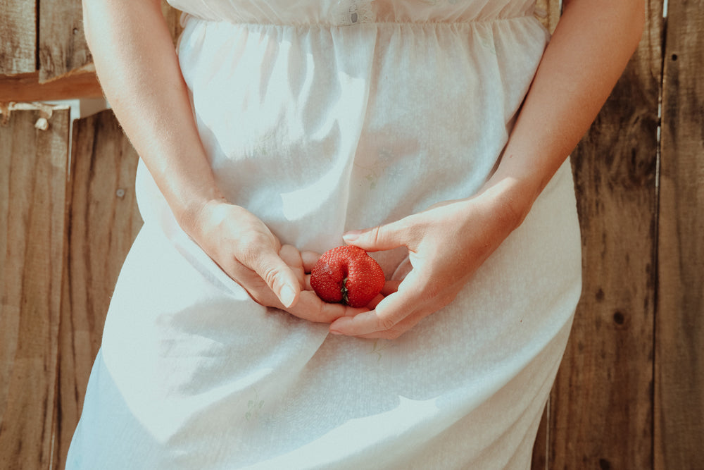 A woman in a white dress gently holding a strawberry.